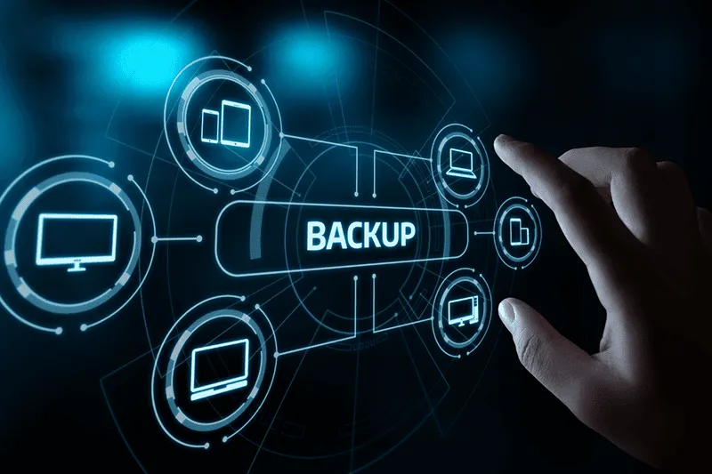 A hand points to a digital interface displaying the word "BACKUP" surrounded by icons of computers and storage devices.