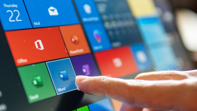 A hand touching a tablet screen displaying colorful app tiles including Mail, Office, Excel, and Word.