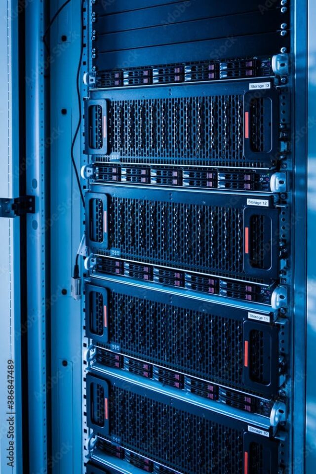 Close-up of a server rack with several stacked servers in a dimly lit room. Cables are visible to the left.