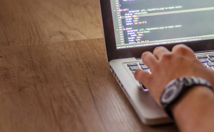 A person typing code on a laptop, with the screen showing lines of programming scripts designed to strengthen cybersecurity.