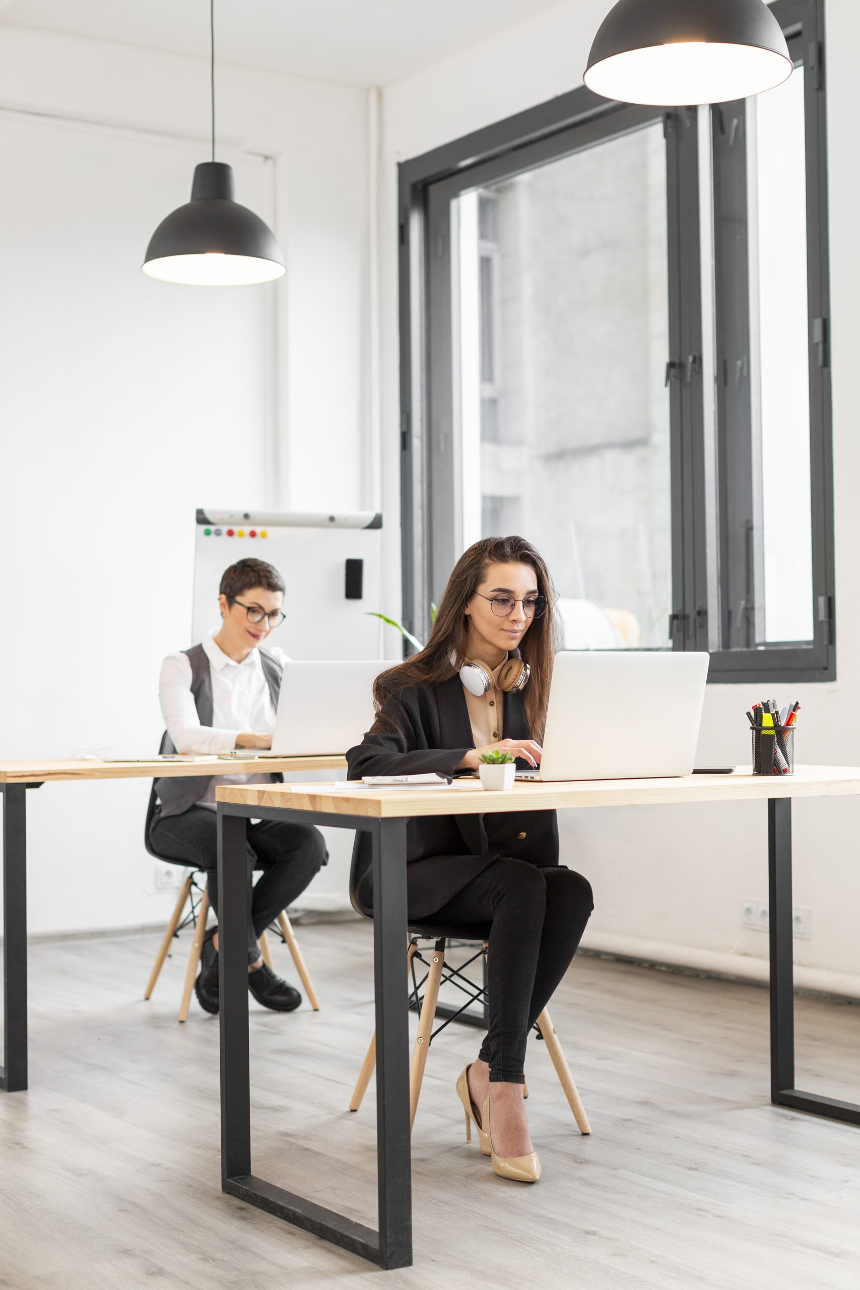 Two people working on laptops in a modern Grand Junction office with large windows and minimalist decor.