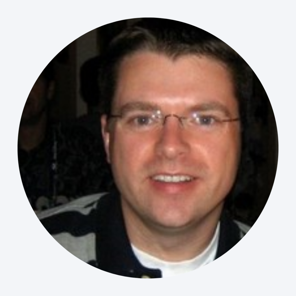 A man with short brown hair and glasses is smiling at the camera, confidently wearing a black and white striped shirt—almost as if ready for an authentication check.