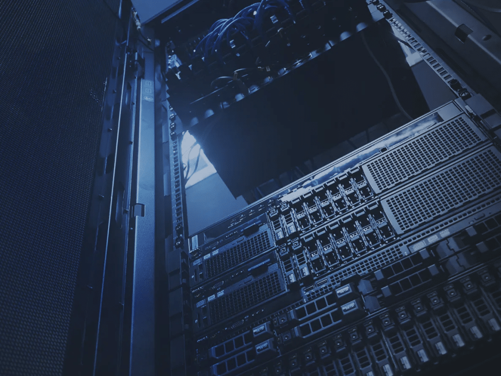 A close-up view of server racks in a data center, showing network cables and hardware components under blue lighting.